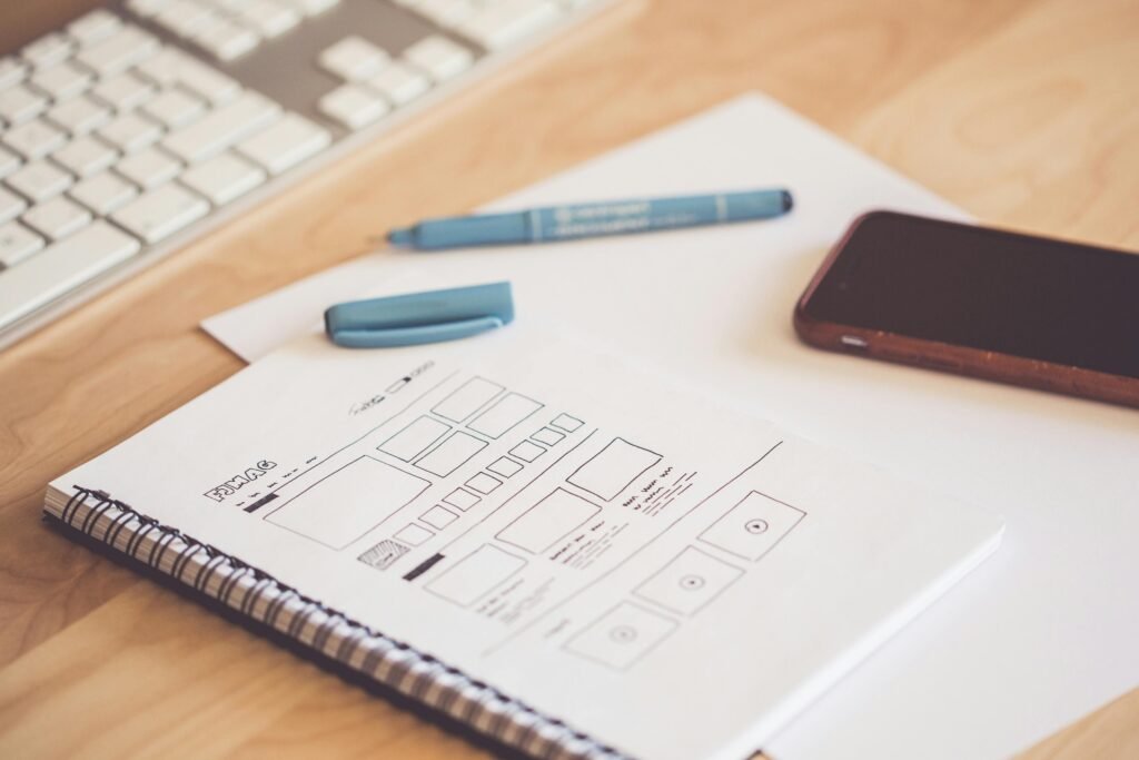 Services A neat workspace featuring a sketchpad with wireframes, a smartphone, and a keyboard on a wooden desk.